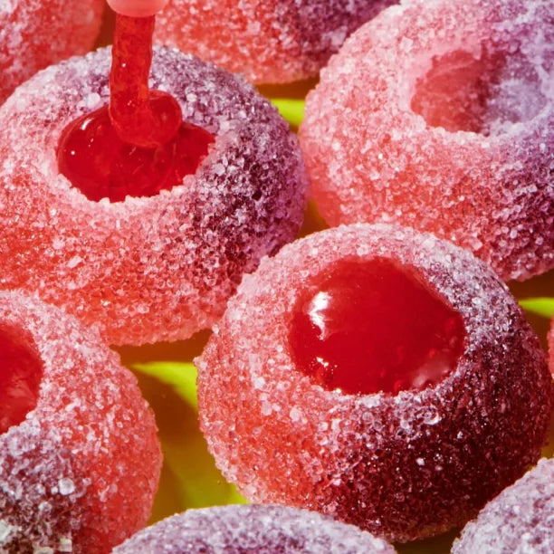 Sugar-coated red jelly candies with a glossy red jelly center, shown in a close-up arrangement with a hand dipping one.