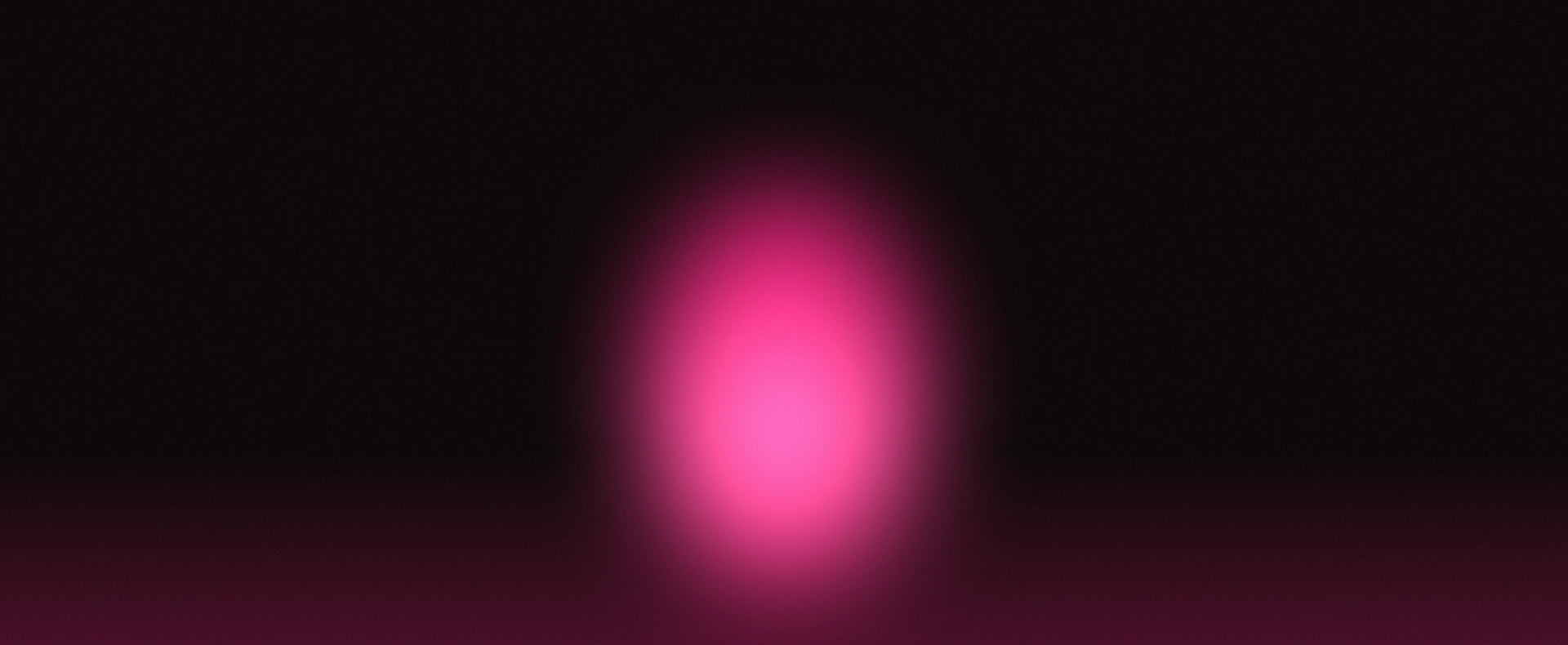A soft, out-of-focus pink oval light glowing against a very dark black background.